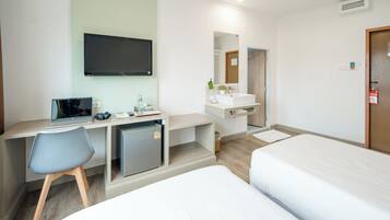 Une chambre d’hôtel équipée d’un bureau, d’une chaise, d’un lit, d’une télévision, d’un lavabo et d’un miroir.