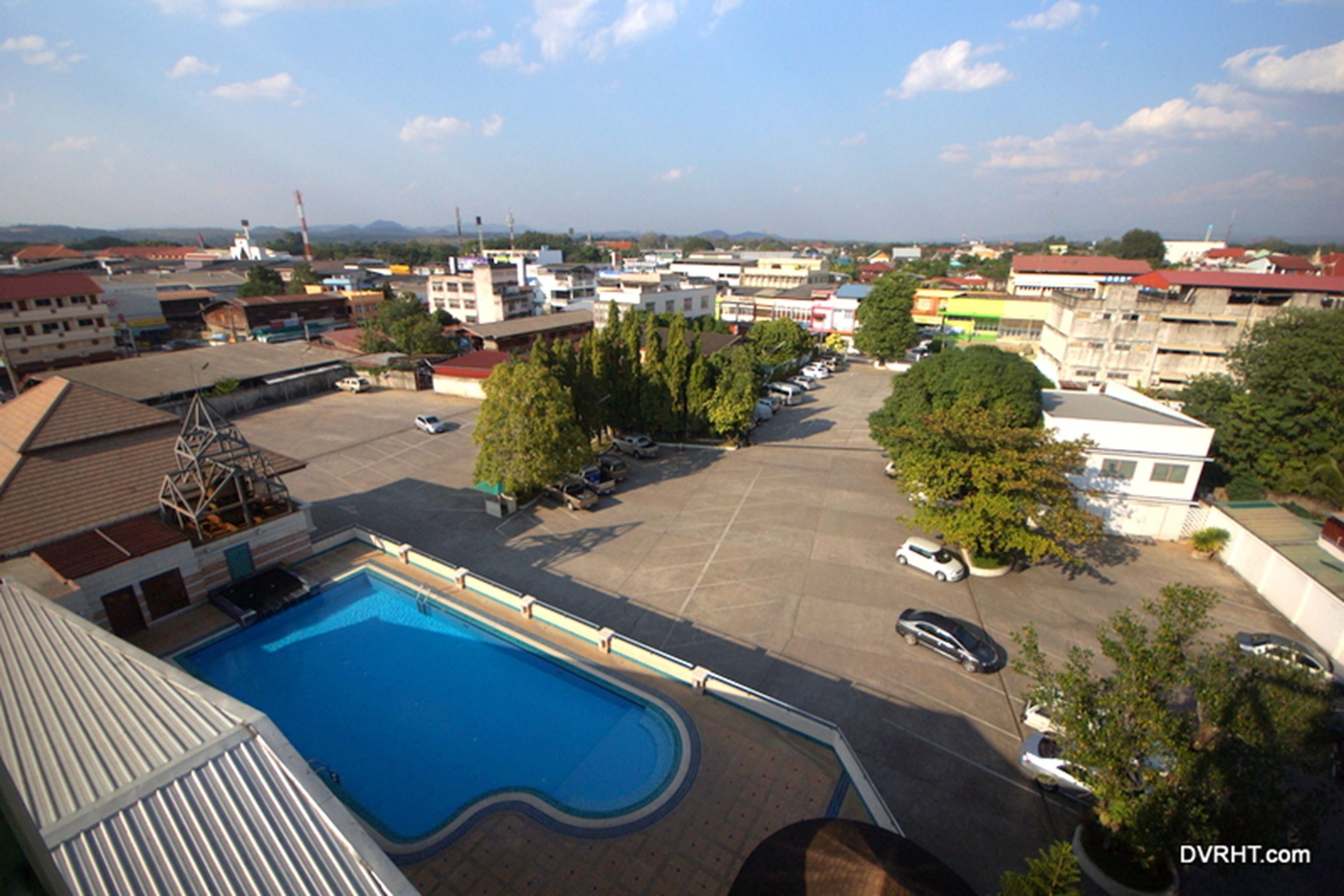 A swimming pool with a surrounding parking area and buildings in the background.