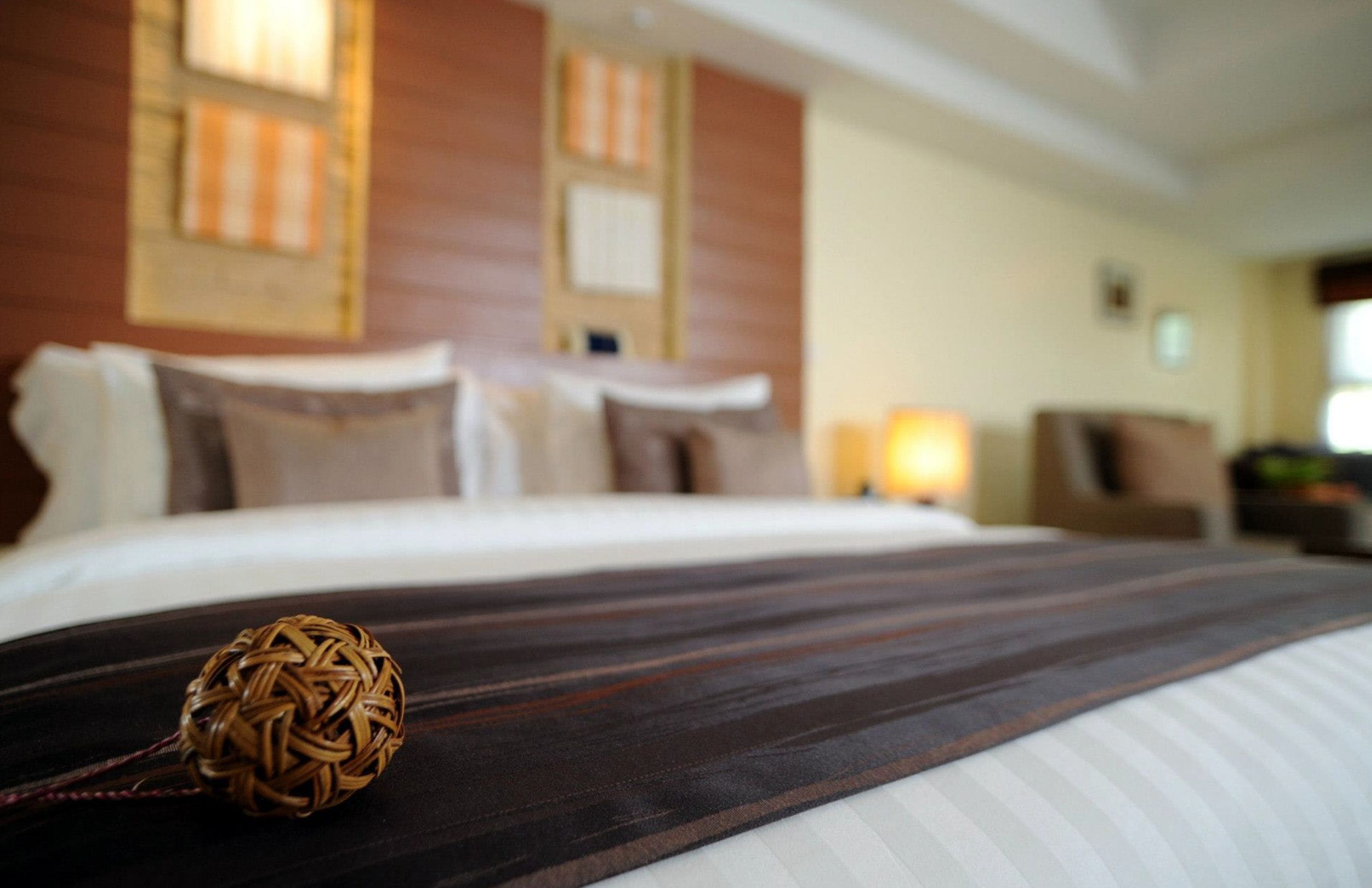 A hotel room with a neatly made bed, a decorative woven ball on the bed, and a view of the room's interior including a window and a wall with a striped pattern.