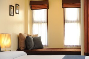 Quarto de hotel com cama, um assento junto à janela com almofadas e uma luminária.
