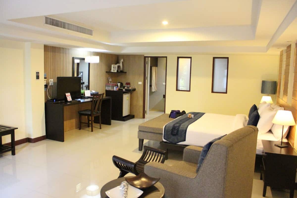 A hotel room with a bed, a desk, a chair, a sofa, and a small kitchenette.