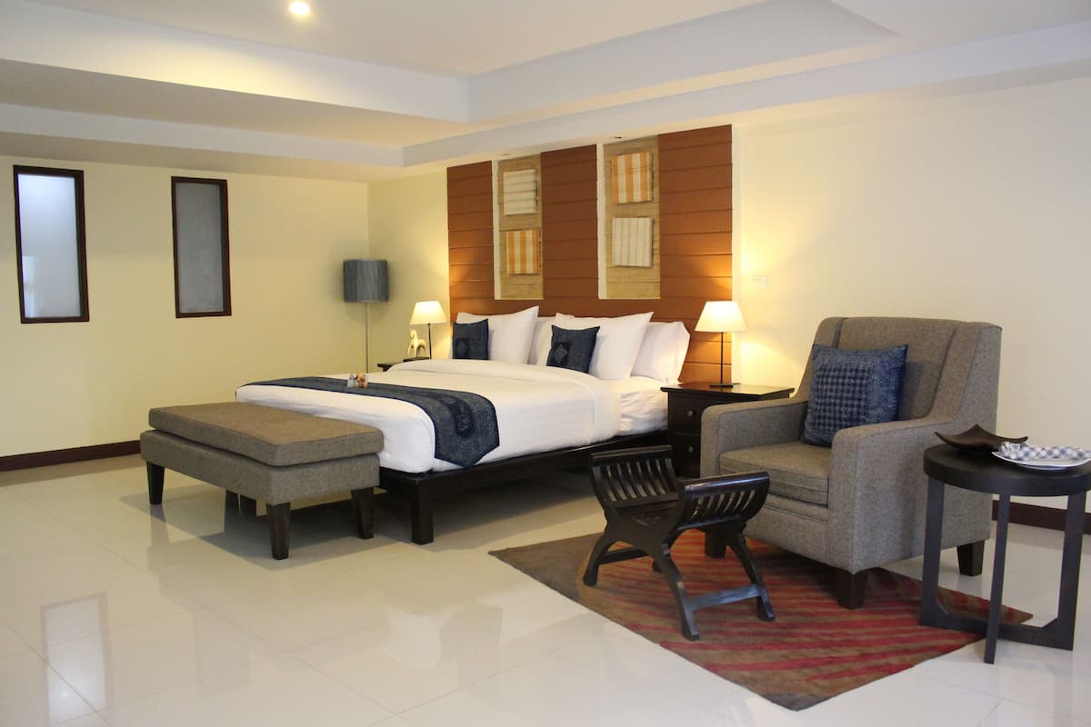 A hotel room with a large bed, a sofa, a small table, and a bench.