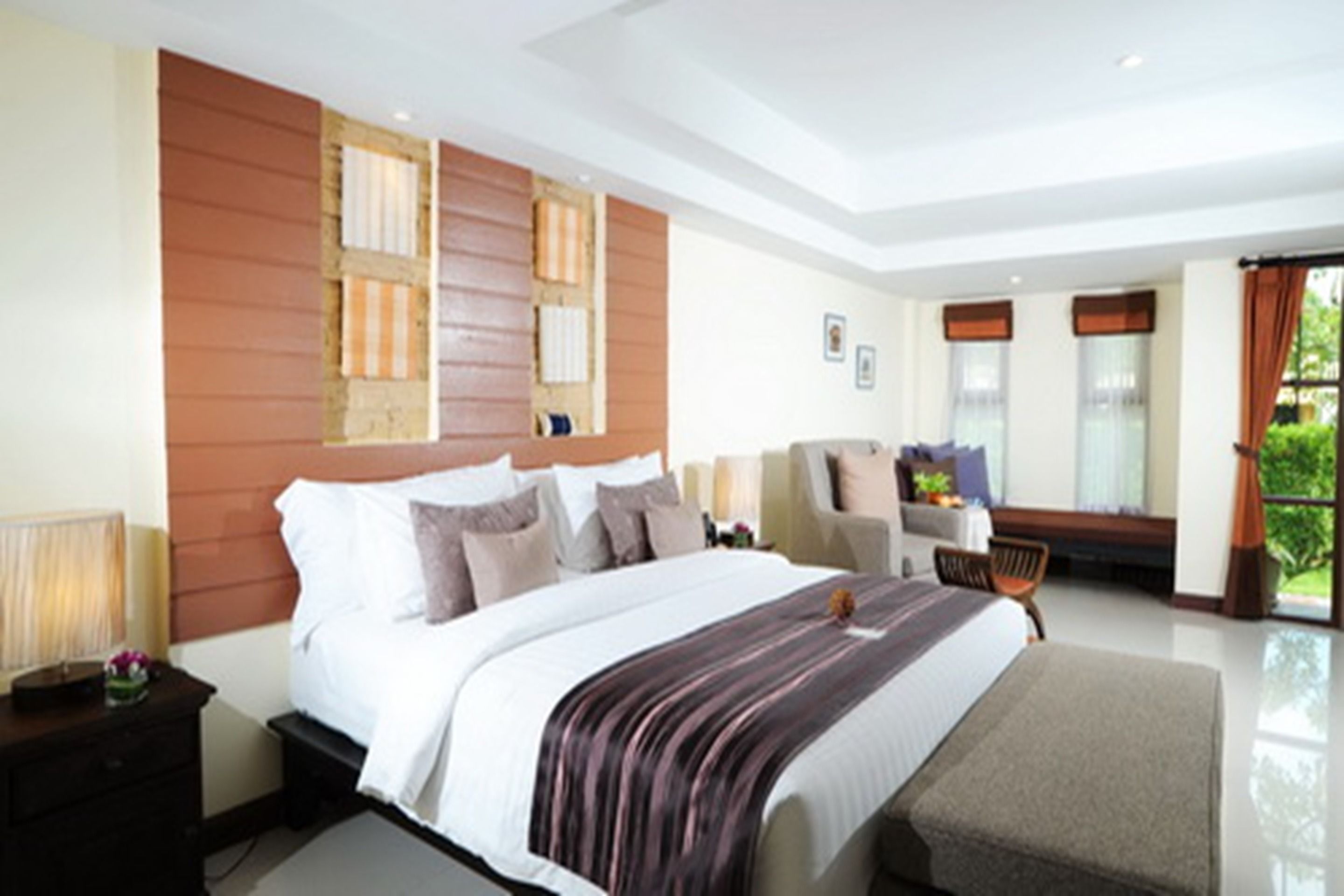 A modern hotel bedroom with a large bed, a desk, and a view of greenery.