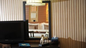 Habitación de hotel con un espejo grande que refleja una cama y una lámpara. Hay un escritorio con un televisor, una figurita de caballo y una caja de pañuelos.