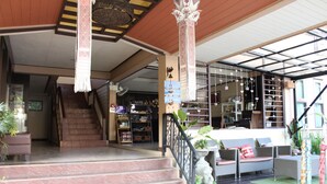 Entrada de hotel con una escalera que conduce a los pisos superiores, un área de recepción con mostrador y un espacio de descanso con cojines y plantas.