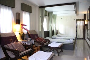 Quarto de hotel com sofá, duas camas de solteiro, uma mesa pequena e um abajur.
