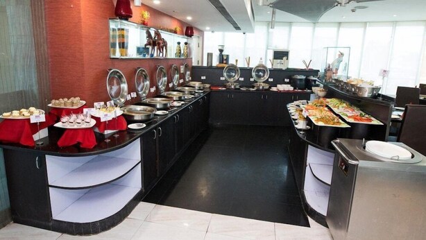 A buffet setup with multiple serving stations, a tiled floor, and a modern kitchen area with stainless steel appliances. - The Theme Jaipur (Jaipur)