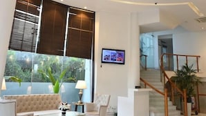 A spacious living area with a large window, a chandelier, a sofa, a coffee table, and a staircase. - The Theme Jaipur (Jaipur)
