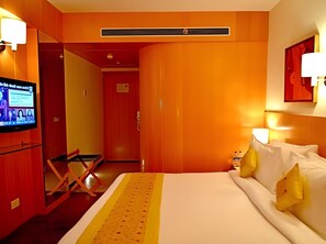 A hotel room with a bed, a television, a desk, and a door. - The Theme Jaipur (Jaipur)