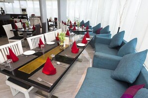 A modern dining area with long tables, blue sofas, and red napkins. - The Theme Jaipur (Jaipur)