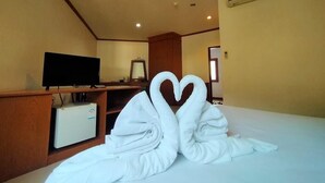 Een hotelkamer met een bed, een televisie op een houten standaard en een handdoek in de vorm van een hart op het bed.