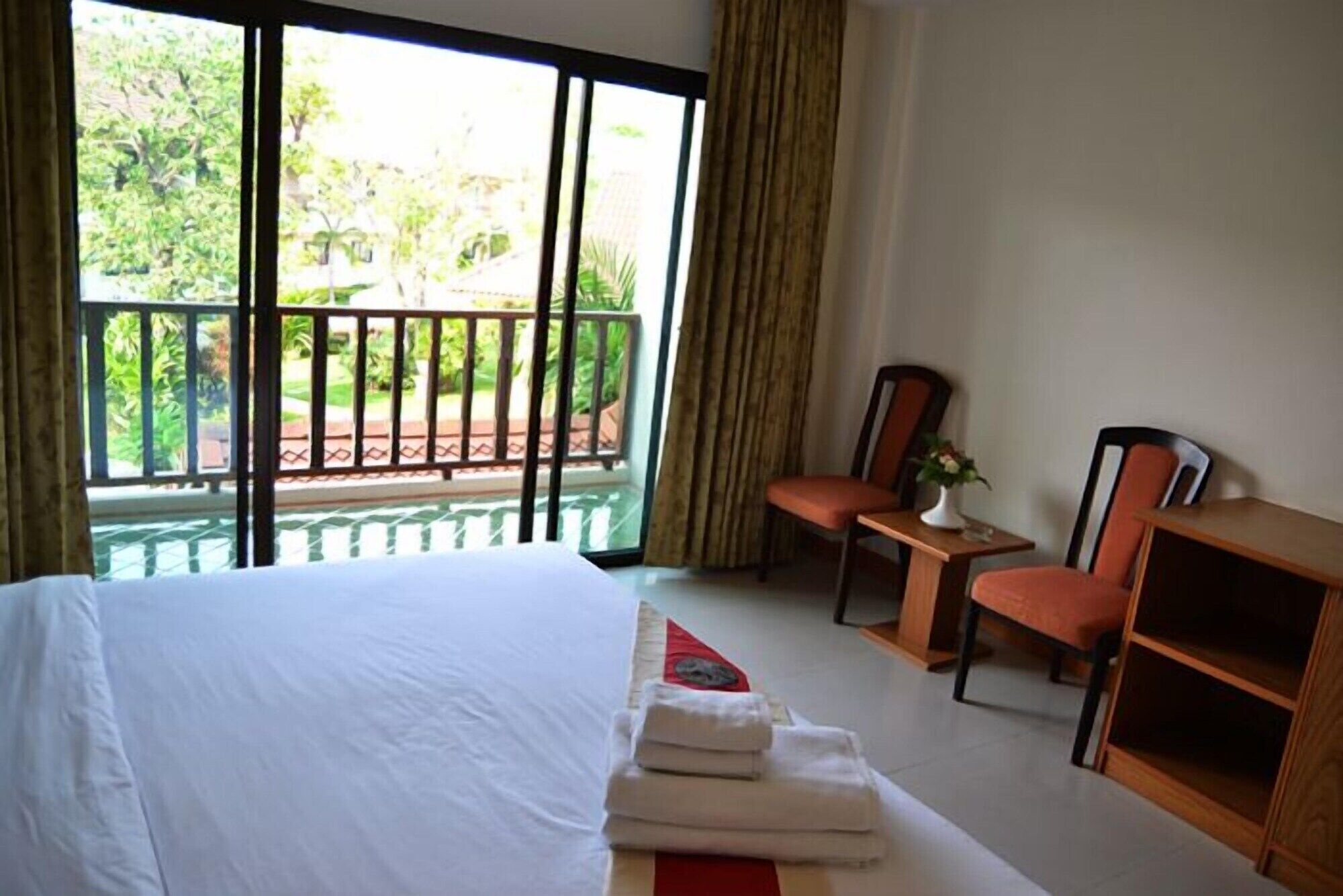 Habitación de hotel con cama, dos sillones, una mesita y vistas a zonas verdes a través de amplios ventanales.