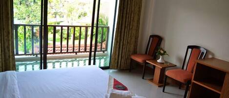 Habitación de hotel con cama, dos sillones, una mesita y vistas a zonas verdes a través de amplios ventanales.