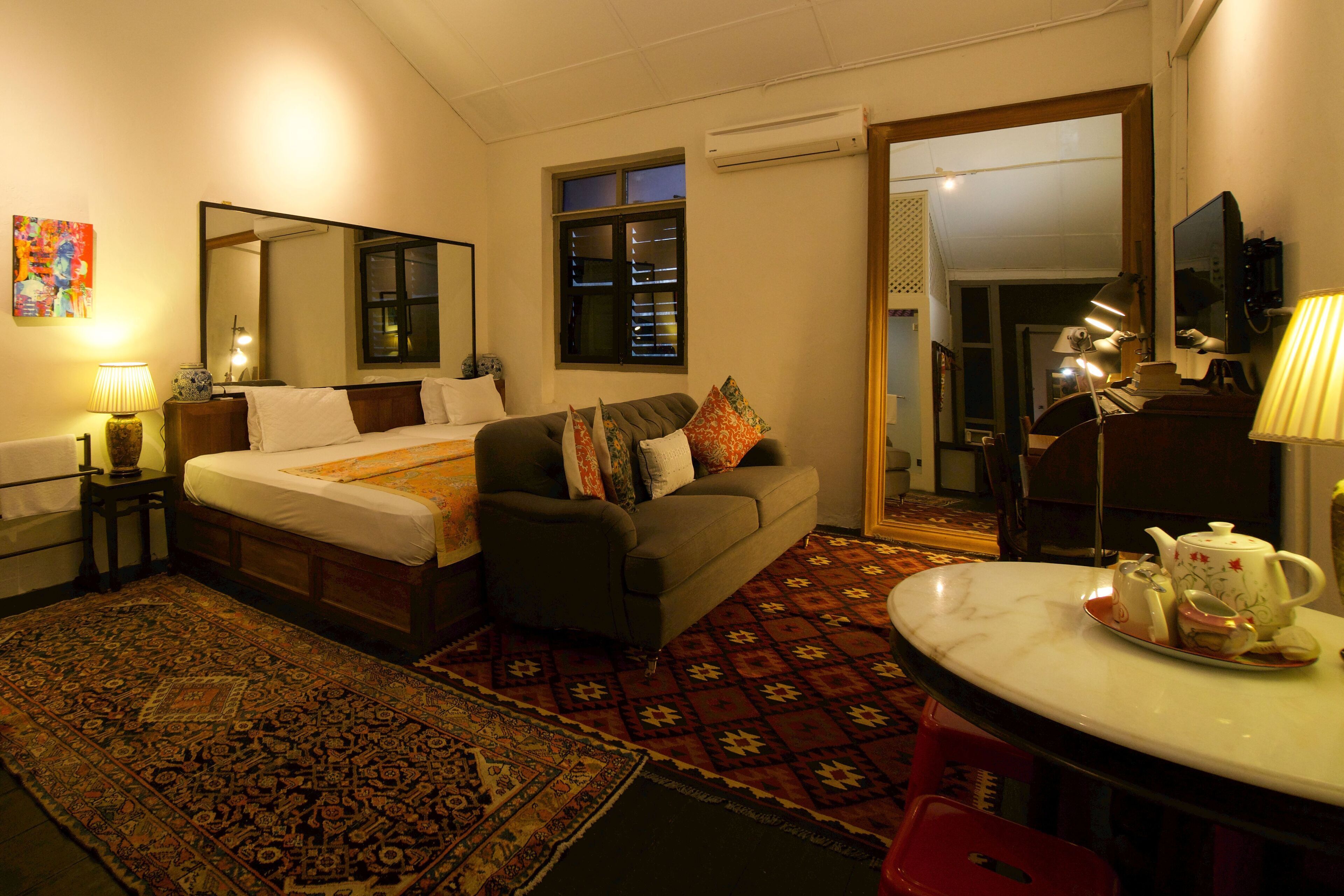 A hotel room with a bed, a sofa, a dining table with tea set, a mirror, and a window.