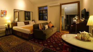 A hotel room with a bed, a sofa, a dining table with tea set, a mirror, and a window.