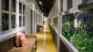 A corridor with a bench and a table, flanked by windows and a railing overlooking a lush garden. - Muntri Mews (George Town)