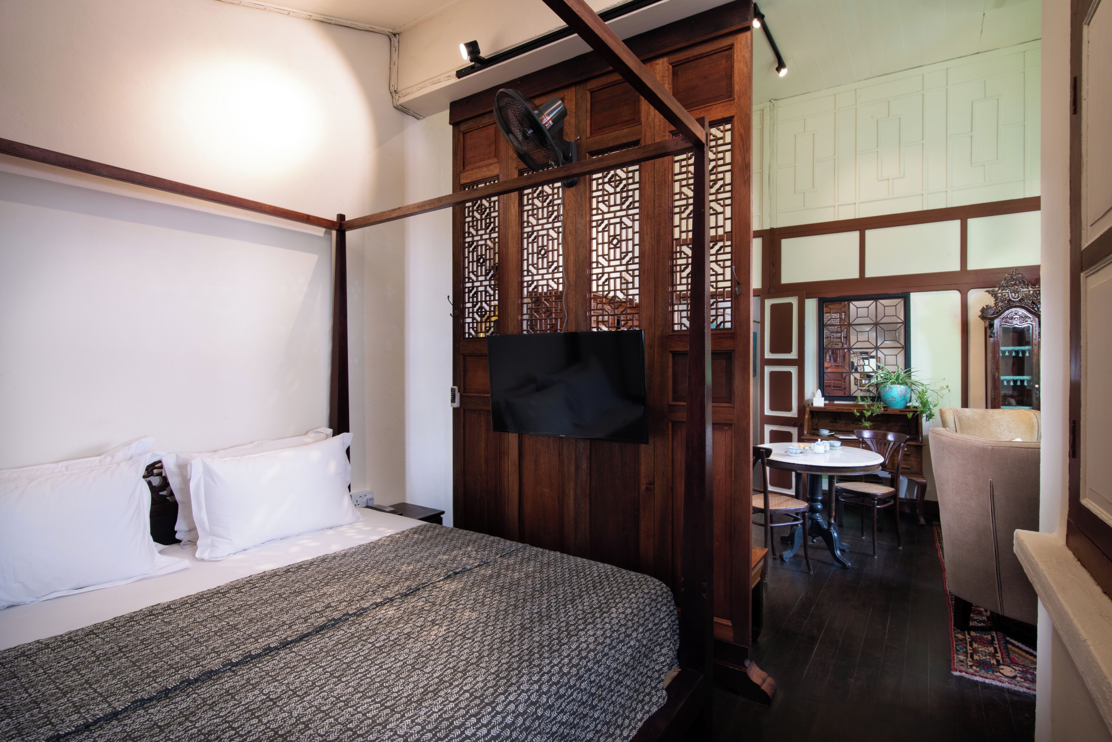 A hotel room with a bed, a TV, a wooden partition, a dining area, and a view of the outside.