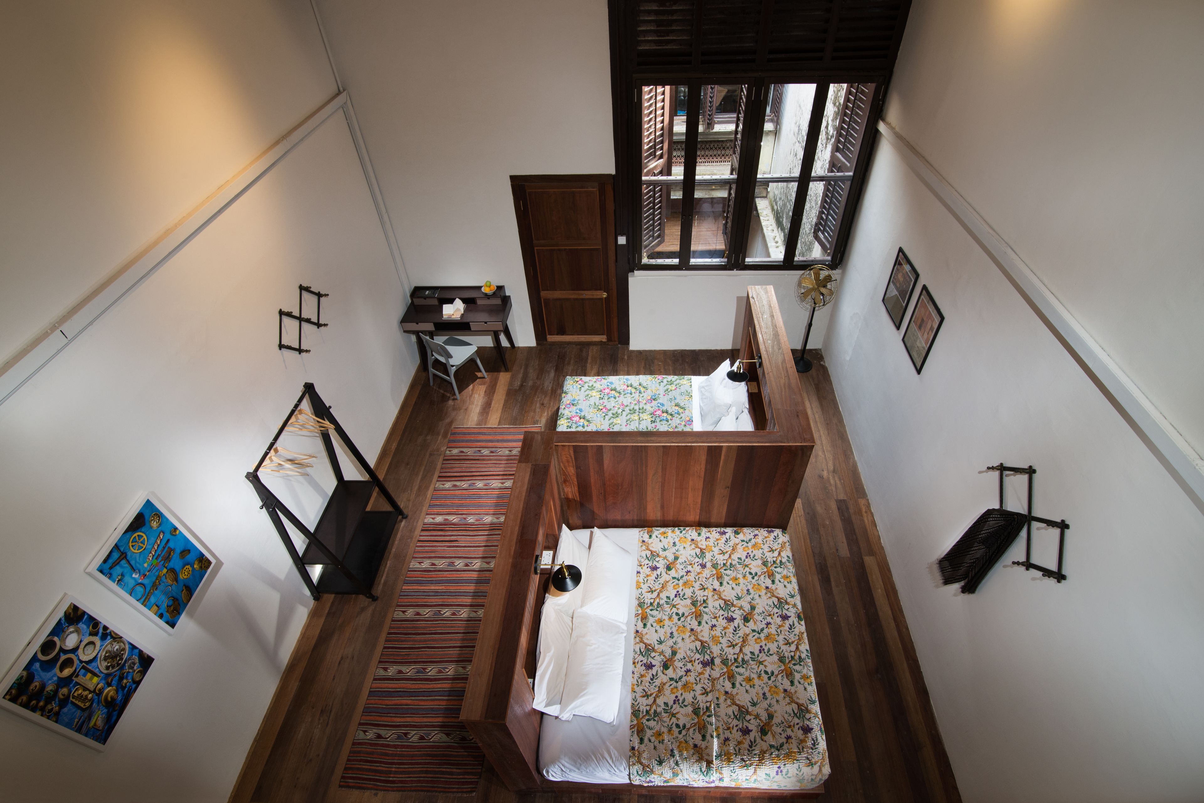 A compact room with two beds, a desk, and a chair. There is a window providing natural light and a view of the outside.