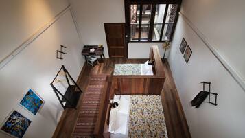 A compact room with two beds, a desk, and a chair. There is a window providing natural light and a view of the outside.