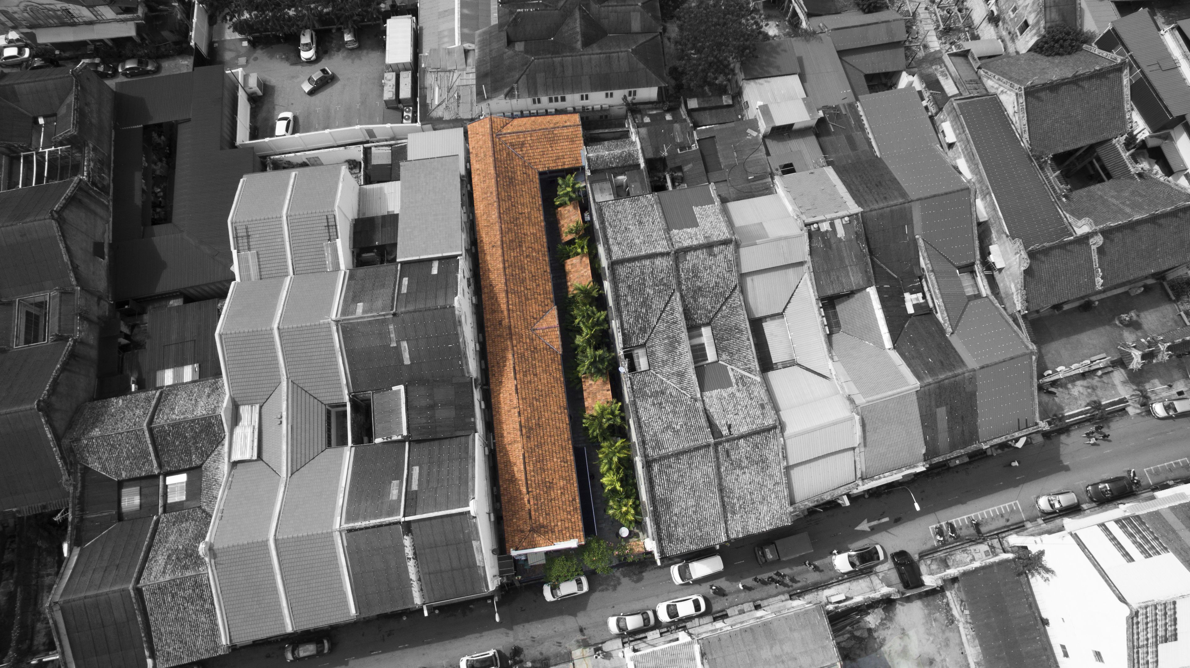 An aerial view of a residential area with a mix of traditional and modern architecture, featuring a prominent building with a unique roof design and a narrow central courtyard.