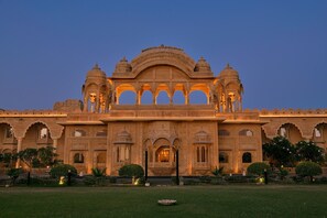A grand building with intricate architecture, featuring multiple domes and arches, and a well-maintained garden in front.
