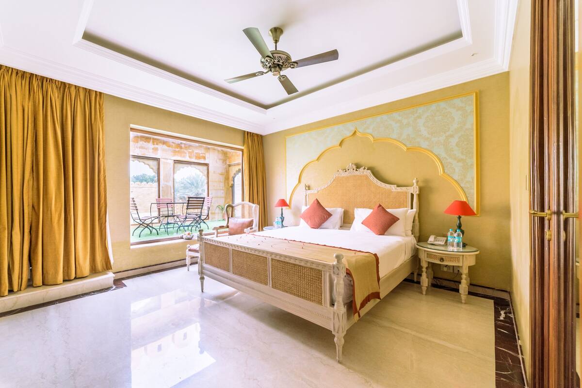 A hotel room with a large bed, a ceiling fan, a window with curtains, and a view of the outside.