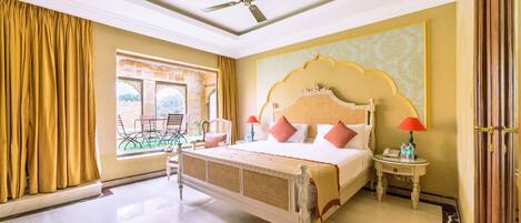 A hotel room with a large bed, a ceiling fan, a window with curtains, and a view of the outside.