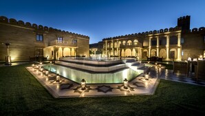 Un patio central con una piscina, rodeado por un edificio con ventanas de arco y suelo de baldosas.