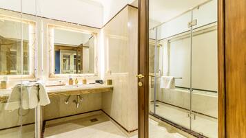 Un baño moderno con cabina de ducha de vidrio, tocador de mármol y un espejo grande.