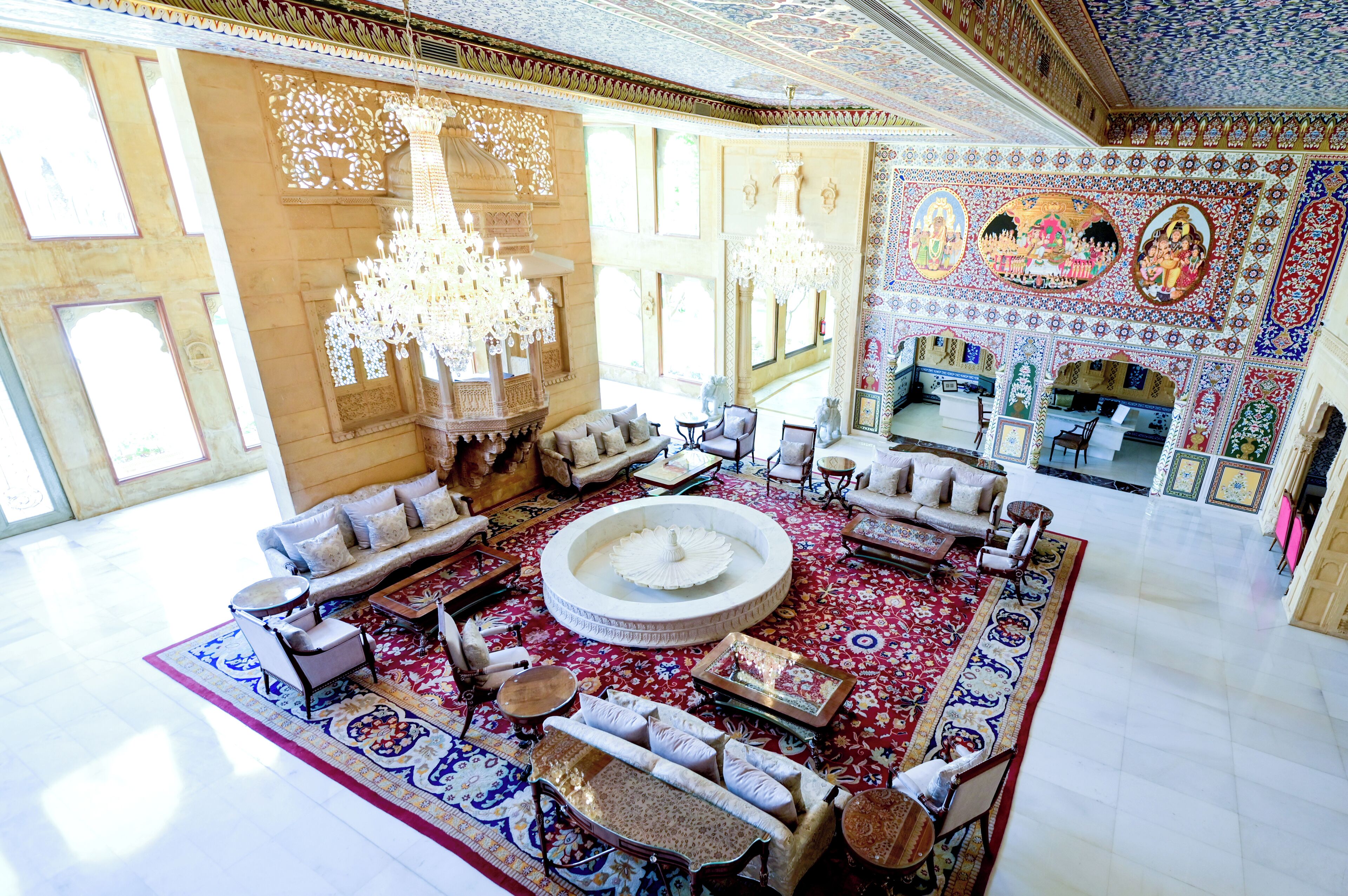 A spacious lobby with a central fountain, ornate chandeliers, and a richly decorated wall with murals.
