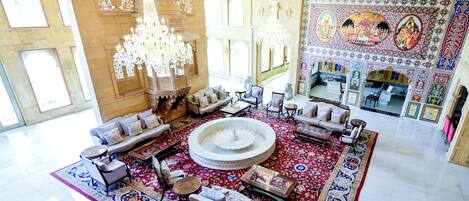 A spacious lobby with a central fountain, ornate chandeliers, and a richly decorated wall with murals.