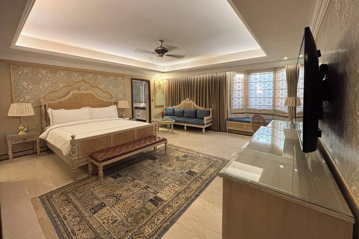A spacious bedroom with a large bed, a sofa, a television, and a ceiling fan.