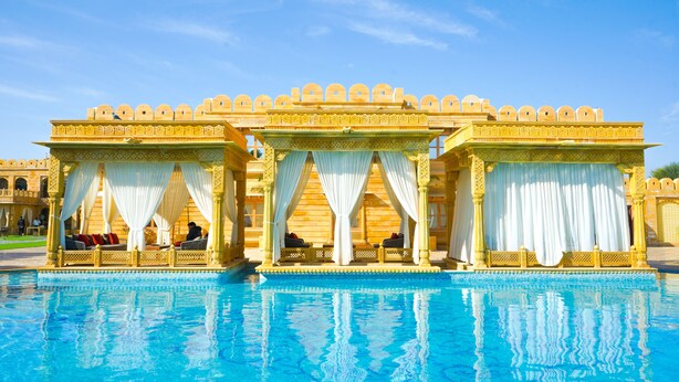 Un área de piscina con una estructura tipo pabellón, asientos y un cielo azul despejado.
