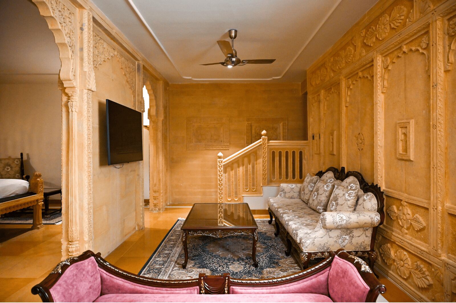A room with a sofa, a coffee table, a TV mounted on the wall, and a staircase.