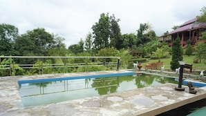 A swimming pool with a stone deck, surrounded by lush greenery and a building in the background. - Ban Rai Tin Thai Ngarm Eco Lodge (Mae Rim)