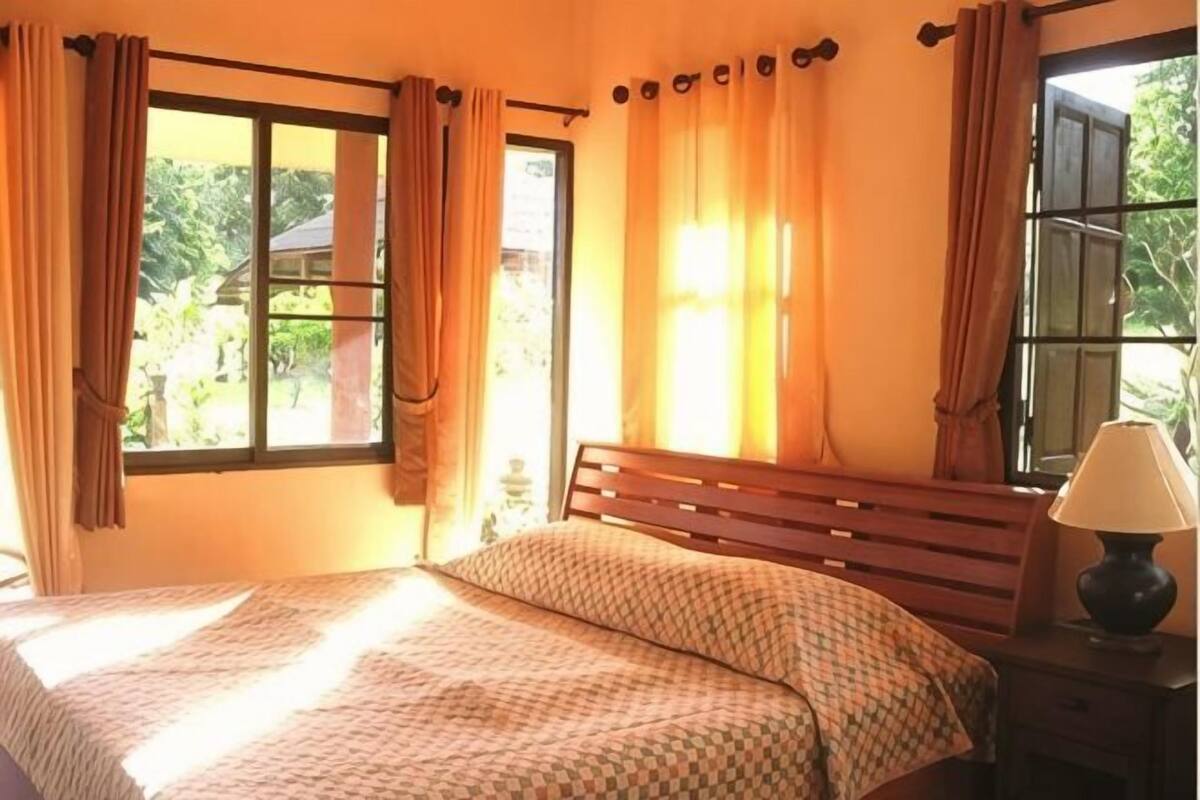 A bedroom with a bed, a nightstand, a lamp, and a window with curtains.