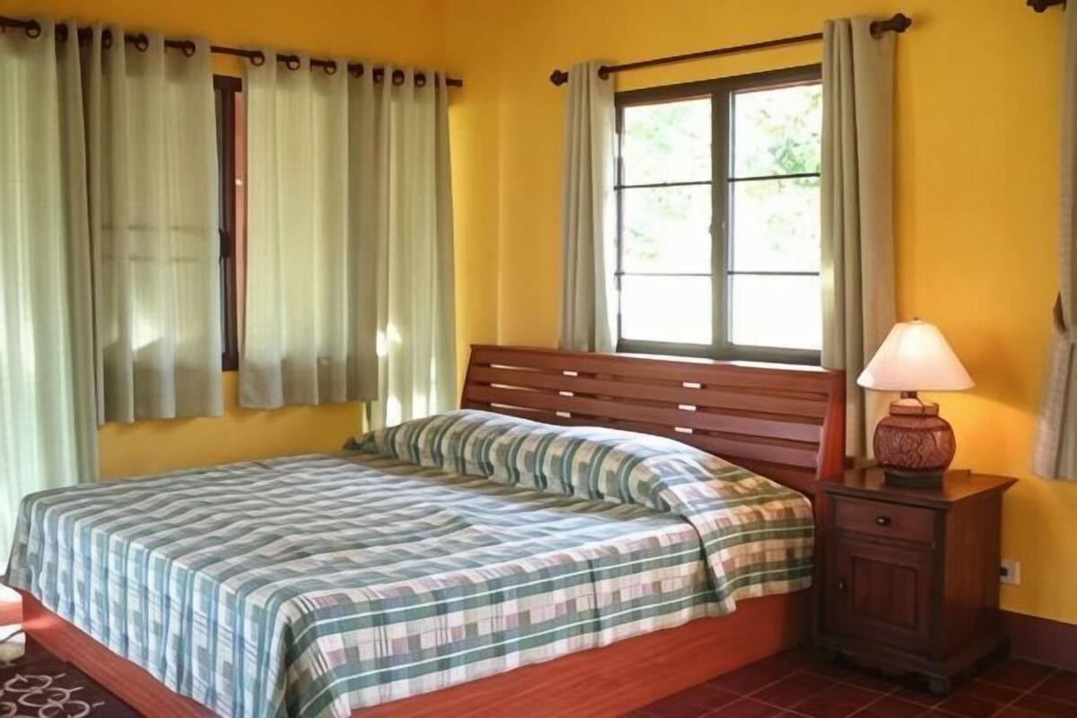 A bedroom with a bed, curtains, a window, and a bedside table with a lamp.
