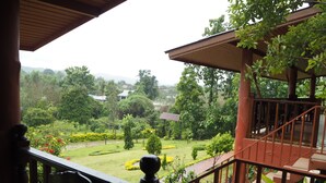 A view from a balcony with a wooden railing, overlooking a well-maintained garden with various plants and a distant view of houses. - Ban Rai Tin Thai Ngarm Eco Lodge (Mae Rim)