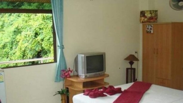 Een slaapkamer met een bed, een televisie op een houten standaard, een kast en een raam met gordijnen.