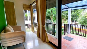 A room with a sofa, a sliding glass door leading to a balcony with a view of greenery and a fence. - Supsangdao Resort (Krabi)