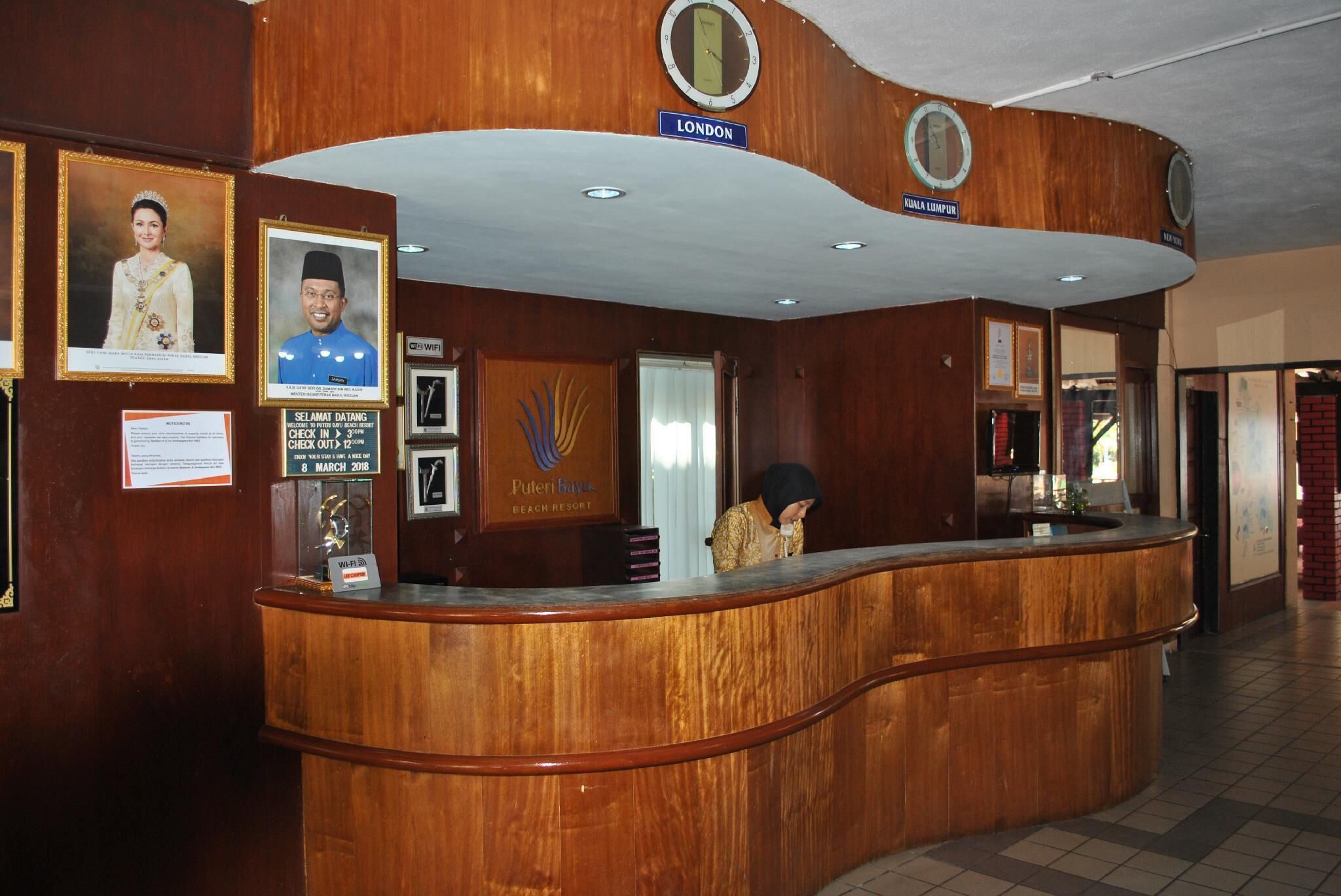 A reception desk with framed photos, a clock, and a sign indicating 'LONDON' and 'KUALA LUMPUR'.