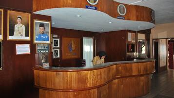 A reception desk with framed photos, a clock, and a sign indicating 'LONDON' and 'KUALA LUMPUR'.