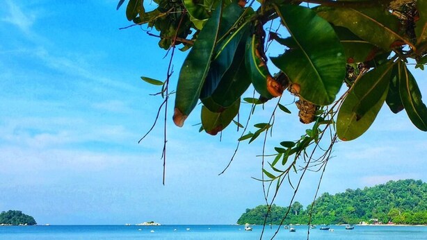 A beach with clear water, boats, and a forested island in the distance. - Puteri Bayu Beach Resort (Kampong Pasir Bogak)