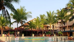 A swimming pool with palm trees, a restaurant, and a building with a red roof. - Puteri Bayu Beach Resort (Kampong Pasir Bogak)