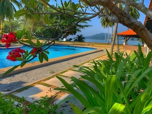 A swimming pool surrounded by tropical plants and a view of the sea.