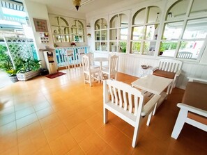 A dining area with white furniture, large windows, and a view of greenery outside. - Chiang Mai Lodge (Chiang Mai)