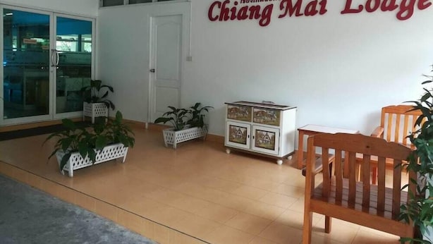 A room with a wooden floor, a white door, and a wall with a sign that reads "Chiang Mai Lodge". There are potted plants and a wooden chair. - Chiang Mai Lodge (Chiang Mai)