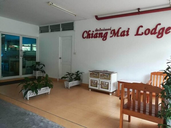 A room with a wooden floor, a white door, and a wall with a sign that reads "Chiang Mai Lodge". There are potted plants and a wooden chair. - Chiang Mai Lodge (Chiang Mai)