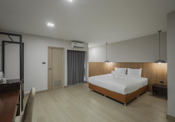 A modern hotel room with a large bed, a desk, a chair, an air conditioning unit, and a ceiling light.