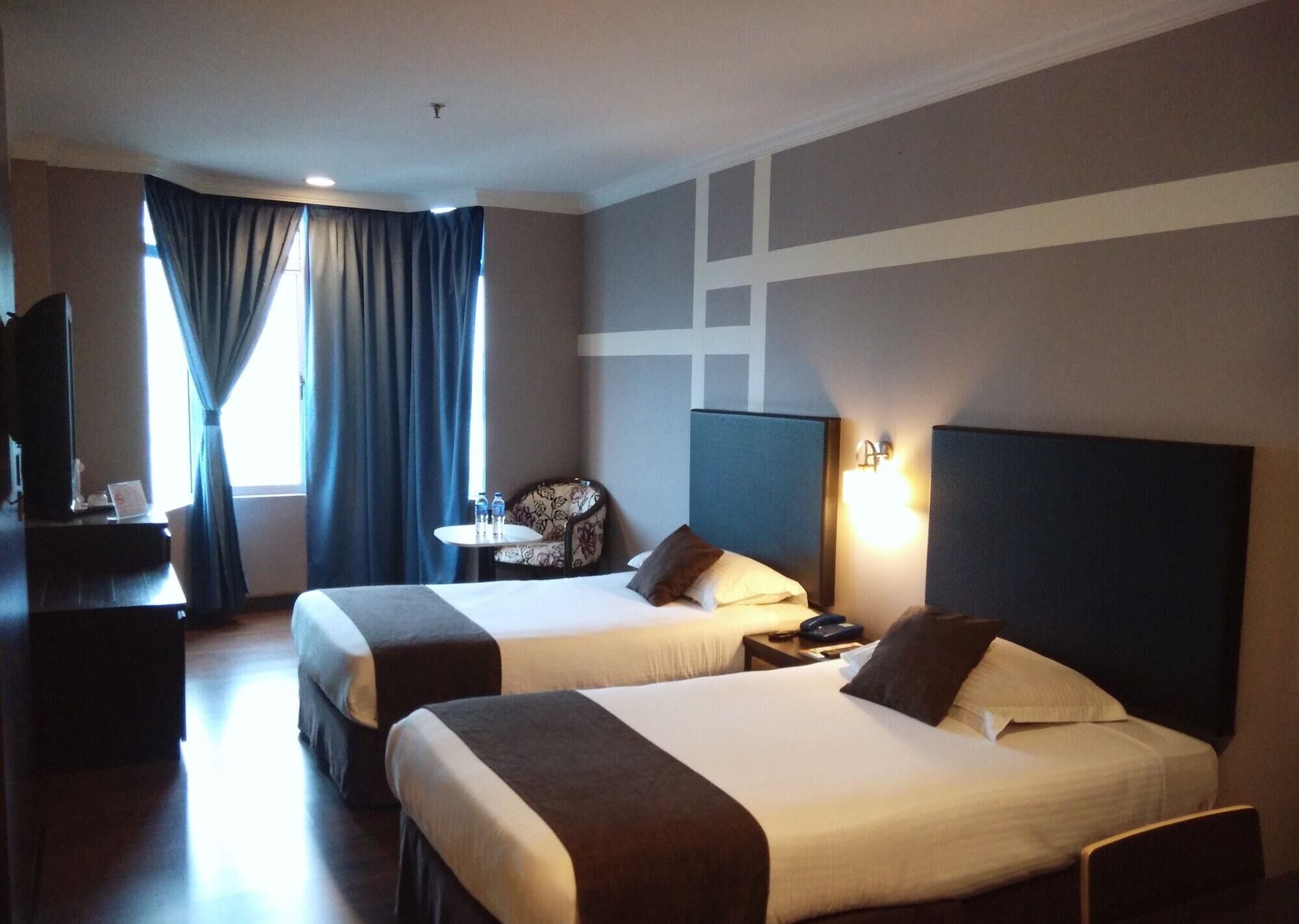 A hotel room with two beds, a desk, a chair, a TV, and a window with curtains.